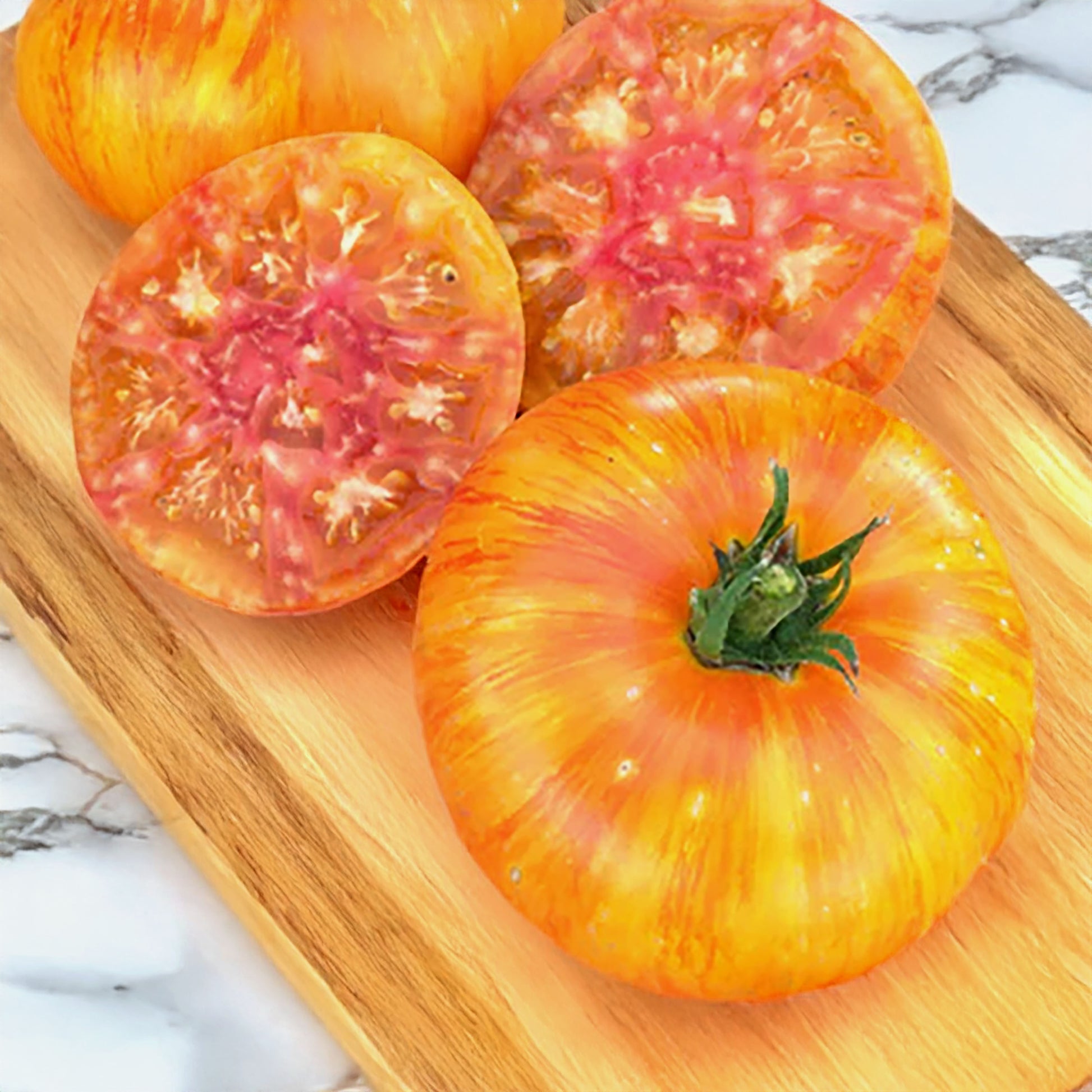 whole orange tomato with red stripes and another cut in half revealing orange, yellow, and red flesh all on a wood cutting board laying on top of a marble counter top 