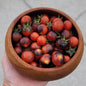 wood bowl filled with cherry tomatoes that are dark red and blue/purple