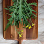 green arugula leaves with yellow flowers laying on a wood cutting board on top of a white marbled countertop